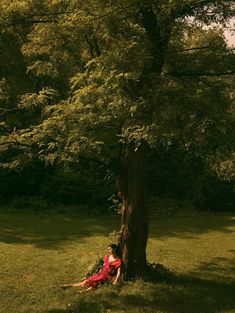 a woman in a red dress sitting under a tree