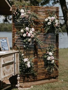 an outdoor ceremony setup with flowers and greenery on the wall, along with a chalkboard sign