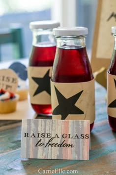 three bottles of raspberry soda on a table with a name tag and cupcakes in the background