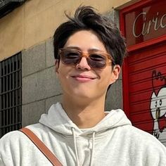 a young man wearing sunglasses standing in front of a red door and holding a brown bag