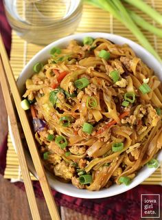 a white bowl filled with noodles and vegetables next to chopsticks on a table