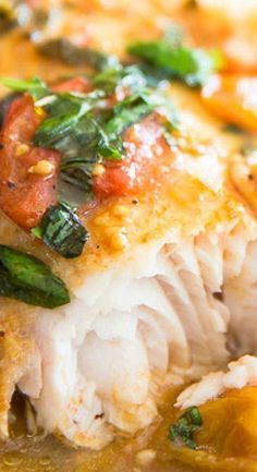 a close up view of some fish in broth with tomatoes and spinach on the side