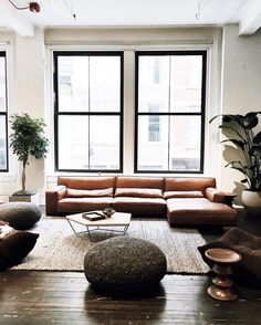 a living room filled with lots of furniture next to large windows and potted plants