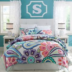 a bed with colorful comforter and pillows in front of a blue wall that has the letter s on it