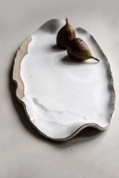 two figurines sitting on top of a white platter with an oval design