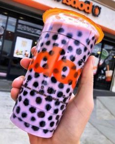 a hand holding up a purple and orange drink in front of a store