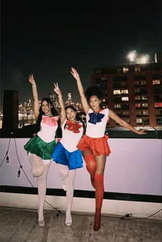 three young women standing on top of a roof with their arms up in the air