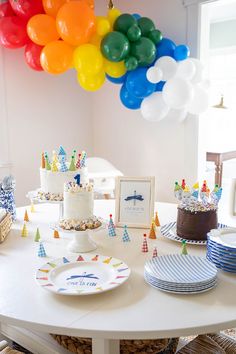 a table topped with lots of cake and colorful balloons hanging from the ceiling above it