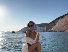 a woman sitting on top of a boat in the ocean wearing a white swimsuit