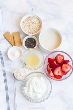 ingredients to make strawberry shortcakes laid out on a white marble counter top, including strawberries, oatmeal, and milk