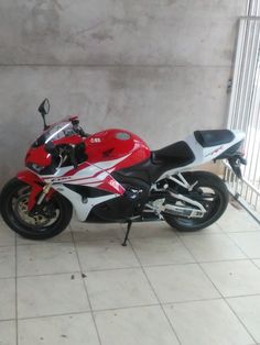 a red and white motorcycle parked next to a wall in a room with tile flooring