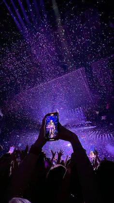 someone holding up their cell phone to take a photo of the stage with confetti all around them