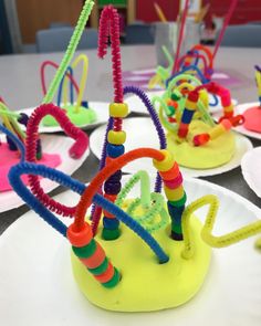 several colorful objects are sitting on plates with scissors and thread spools sticking out of them