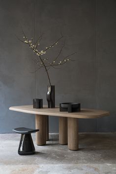 an elegant dining table with two chairs and a vase on it, in front of a gray wall