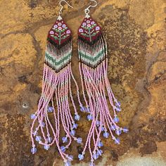 two pairs of beaded earrings with pink and green fringes on top of a rock