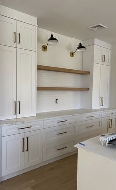 an empty kitchen with white cabinets and wood flooring on the countertop, along with two lights