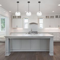 a large kitchen with white cabinets and an island in the middle of the room is lit by three pendant lights