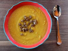 a red bowl filled with soup next to two spoons on top of a wooden table