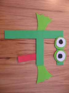 the letter t is made out of paper with googly eyes and a green leaf