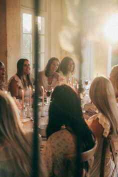 a group of women sitting around a dinner table with candles in the middle of them