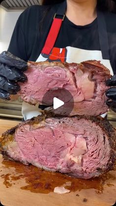 a woman holding two large pieces of meat on top of a wooden cutting board