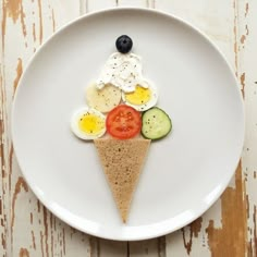 a white plate topped with an ice cream cone covered in fruit and veggies