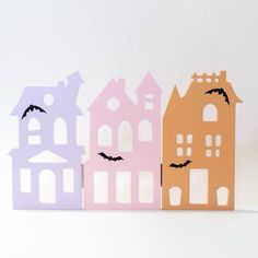 three paper houses with bats on them are lined up against a white background, one is pink and the other is orange