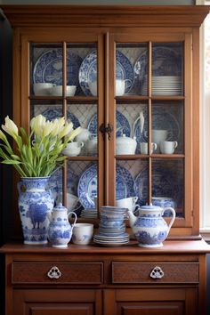 a blue and white china cabinet with flowers in it's vases on top