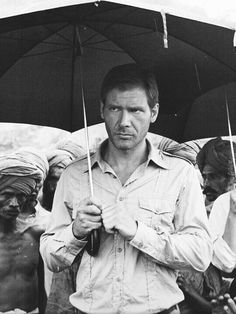 a man holding an umbrella over his head while standing next to other men in the rain