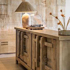 a table lamp sitting on top of a wooden cabinet next to a vase with flowers