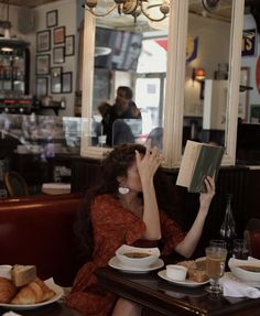 a woman reading a book while sitting at a table in a restaurant with food on it