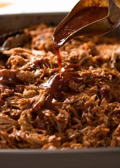 someone pouring barbecue sauce on pulled pork in a pan