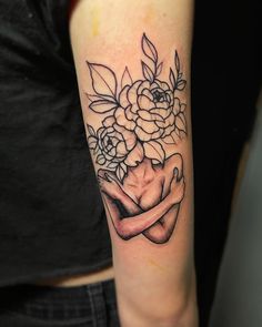 a woman's arm with flowers on it and her hand holding something in the middle