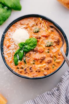 a close up of a bowl of soup on a table with bread and basil leaves