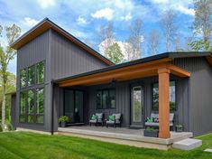 a house that is in the grass with some chairs on the front porch and covered patio area