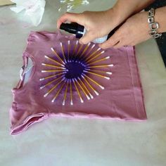 a woman is using an airbrush to paint a t - shirt with purple and yellow designs