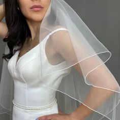 a woman wearing a white wedding dress with a veil on her head is posing for the camera