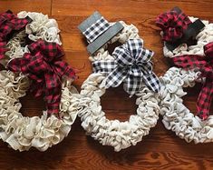 three wreaths with plaid bows on them sitting on a wooden floor next to each other