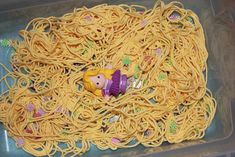 a plastic container filled with yellow noodles covered in little princess dolls and other things on top of it