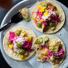 three tortillas on a plate with pickles, cabbage and other toppings