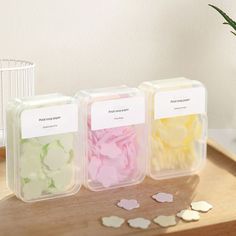 three plastic containers filled with flowers on top of a wooden table next to a potted plant