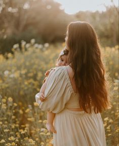 a woman holding a baby in her arms while standing in a field full of flowers