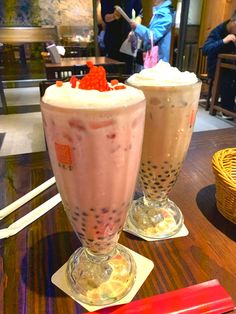 two drinks sitting on top of a table with strawberries in the cup next to them