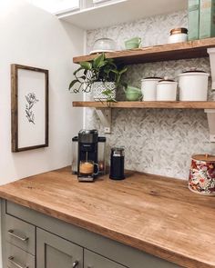 a kitchen counter with coffee maker, potted plant and mugs on it's shelves