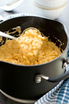 a ladle full of macaroni and cheese being stirred with a spoon in a skillet