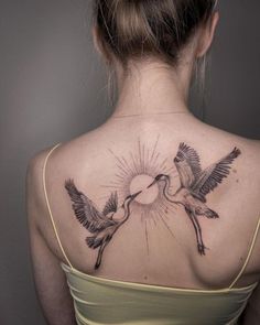 the back of a woman's neck with two birds flying towards eachother