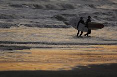 two surfers walking into the ocean with their surfboards in hand at sunset or dawn