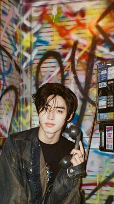 a young man holding an old phone in front of graffiti covered wall