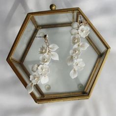 a pair of earrings with white flowers hanging from it's earwires in a hexagonal frame