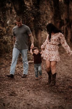 a man and woman holding hands while walking with a small child on a dirt path